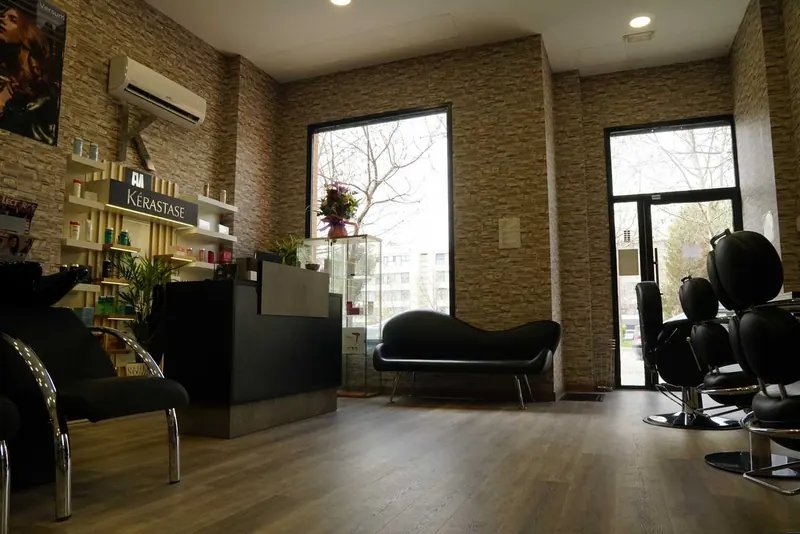 Recepción con mostrador negro, sofá y estantería de productos Kérastase junto a la ventana